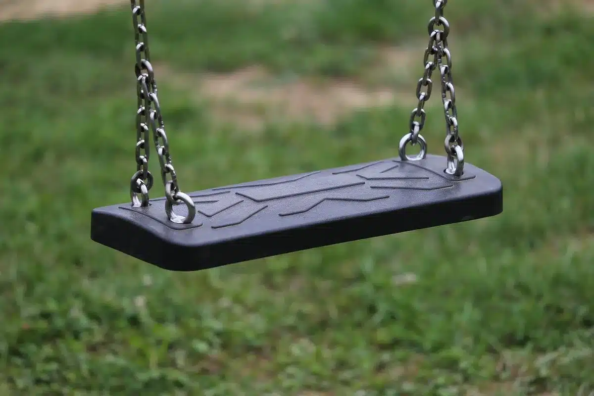 Silhouettierte Hände und eine leere Schaukel auf einem Spielplatz, symbolisch für Trennung und Sorge